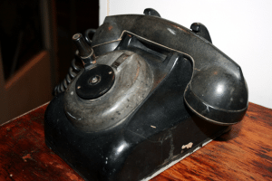 Vintage black rotary phone with a worn, rustic finish highlighting its classic design.